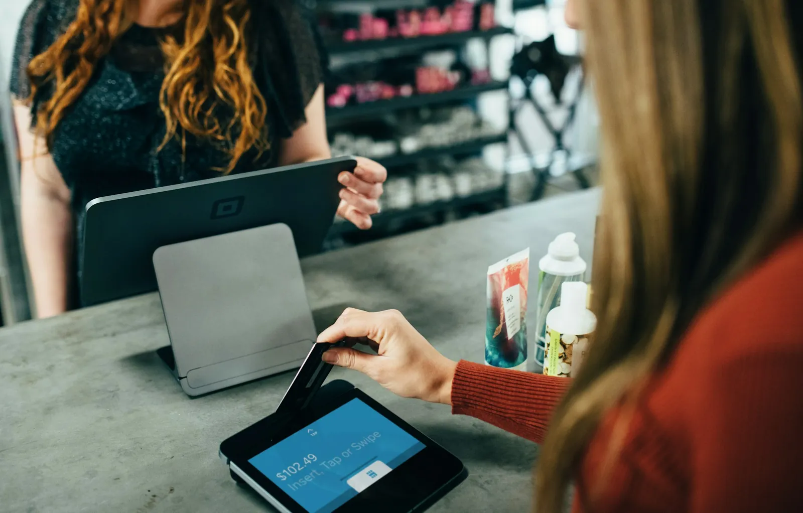 A customer inserts a card into the customer-facing screen of a Square Register at a shop counter while the seller stands behind the register.
