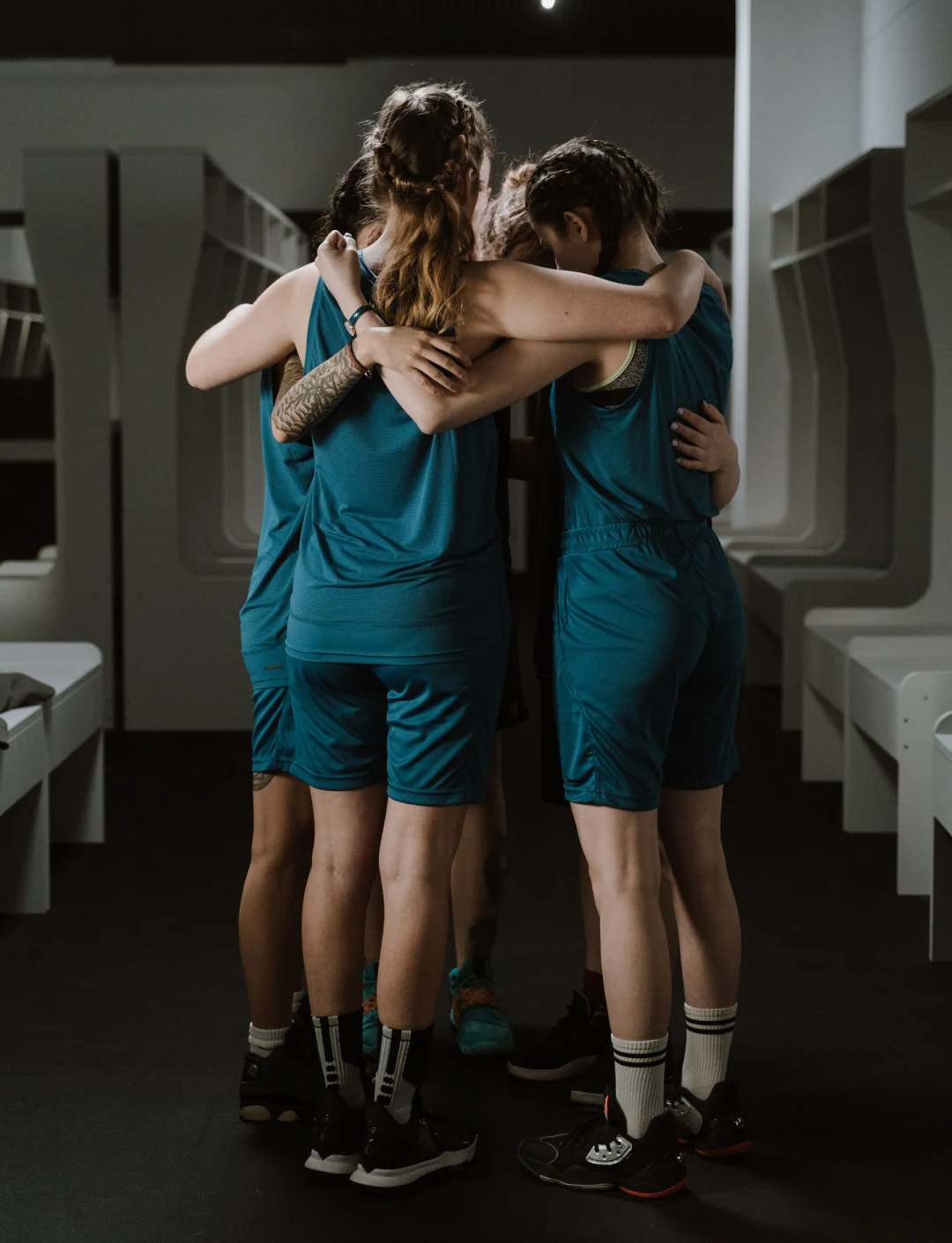 Basketball players in matching teal uniforms gather for a team huddle.