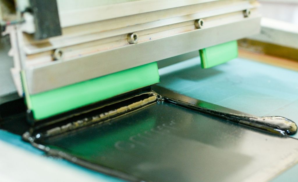 A squeegee pushing black ink on an automatic screen printing machine.