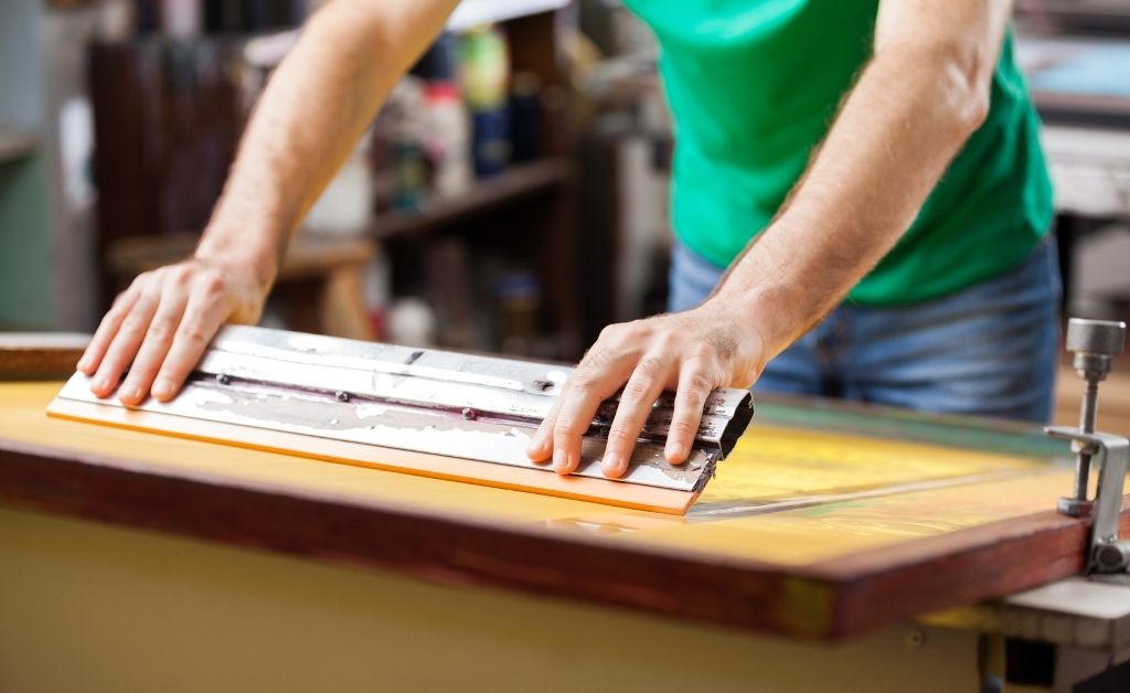A person pushing a long screen printing squeegee.