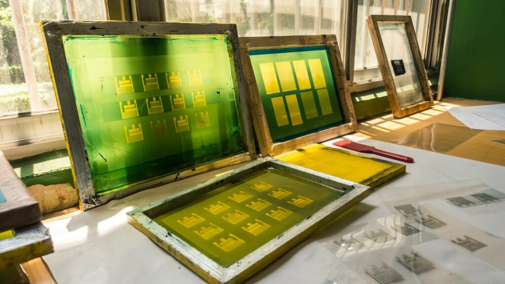 3 screen printing screens laying against a window, and two laying on a floor.