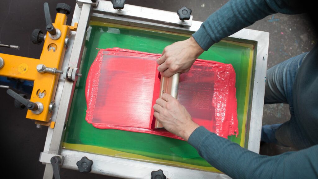 A person using a squeegee to apply inks to the garment