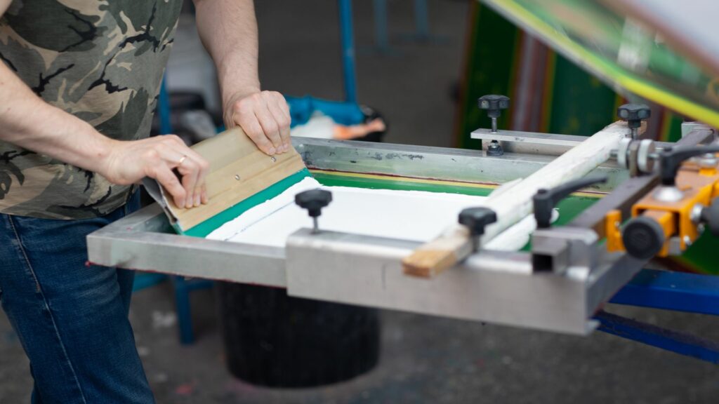 A person using a squeegee to apply inks to the garment on a press