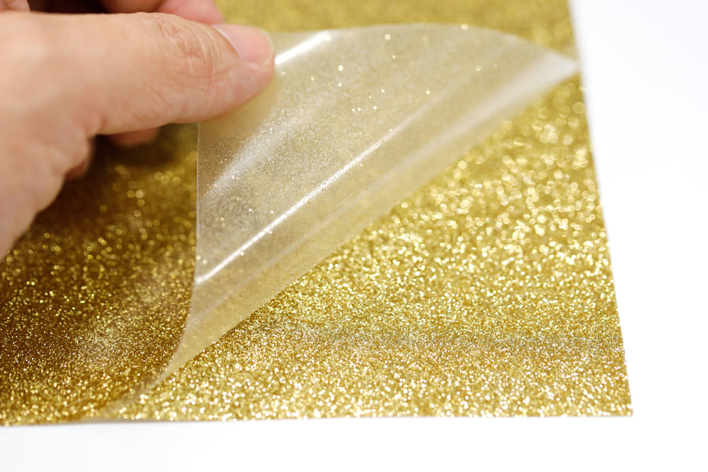 A person peeling a gold glitter heat transfer vinyl sheet
