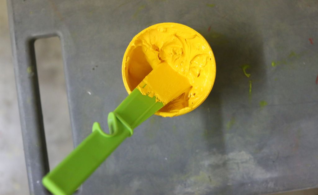 An open bottle of yellow paint with a brush