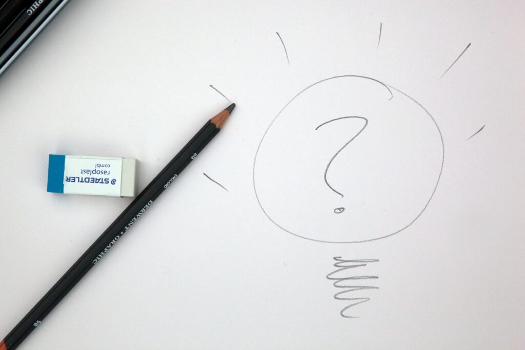 A pencil and eraser laying beside a lightbulb sketch with a question mark in the middle of the bulb