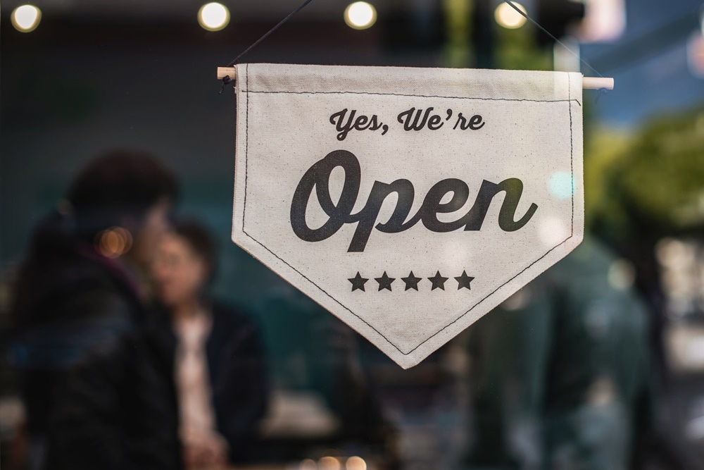 A "Yes, We're Open" sign hanging on a glass door