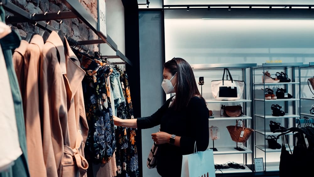 A masked shopper browsing clothes in a store