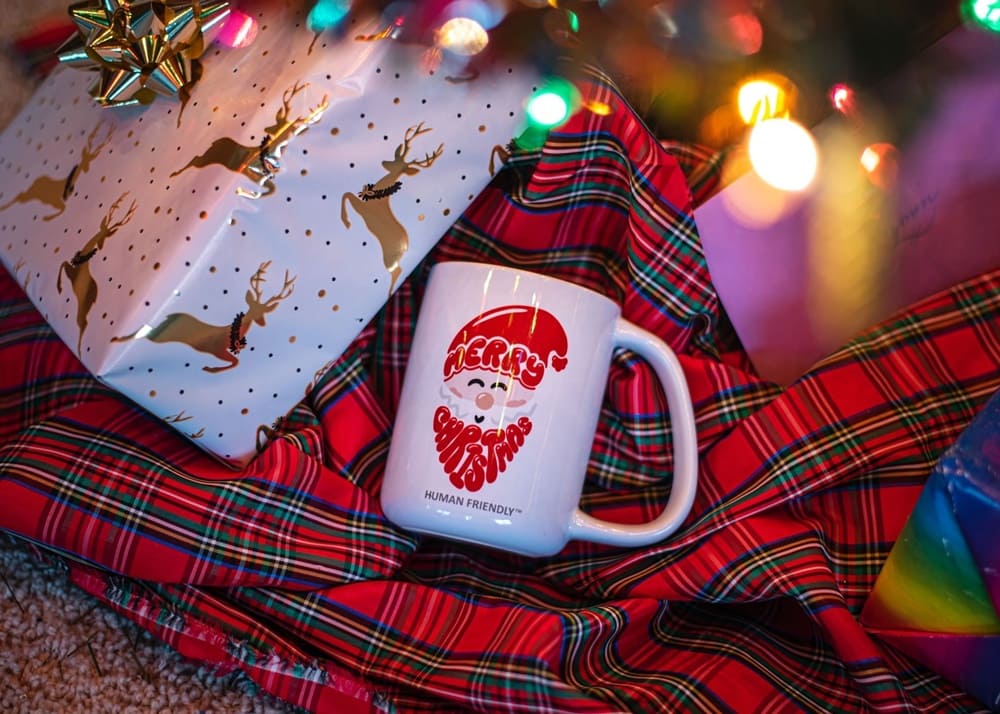 A decorative Christmas mug sits atop a scarf and some wrapped presents