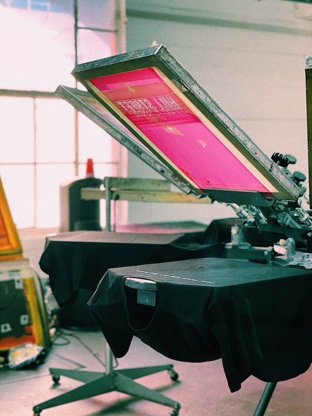 A manual screen printing press with a garment on the platen
